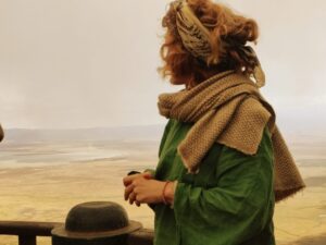 Woman standing at the edge of the Ngorongoro Crater, looking out over the vast green landscape under a cloudy sky, reflecting quietly in nature.