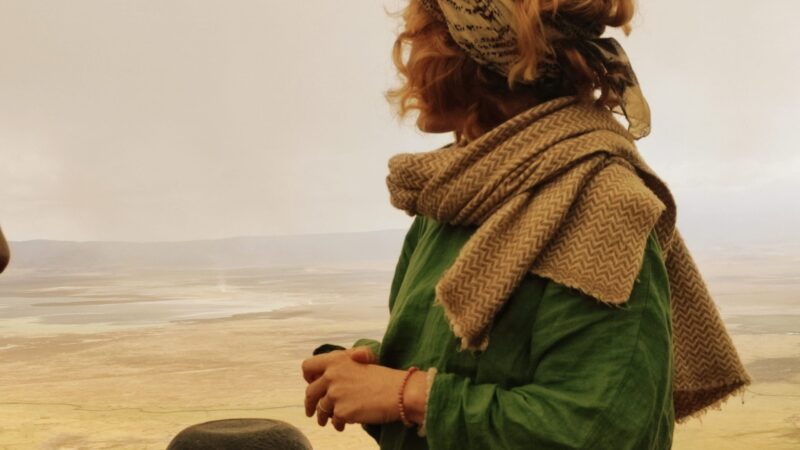 Woman standing at the edge of the Ngorongoro Crater, looking out over the vast green landscape under a cloudy sky, reflecting quietly in nature.