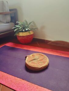 Layered bright pink foam yoga mat with mud stains and a thin purple travel mat in a cozy living-room corner in Tanzania
